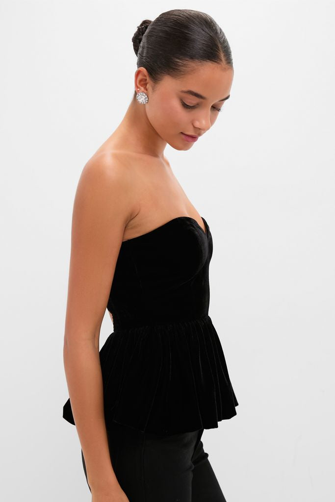 Young woman in profile wearing a classic Black Velvet Peplum Strapless Tudor Blouse, embodying an effortless, high-end style with large stud earrings and a neat bun.