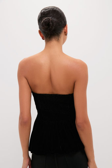 Woman in a sleek bun wearing a Black Velvet Peplum Strapless Tudor Blouse, showcasing its classic, smocked-top design for an effortless, high-end look.