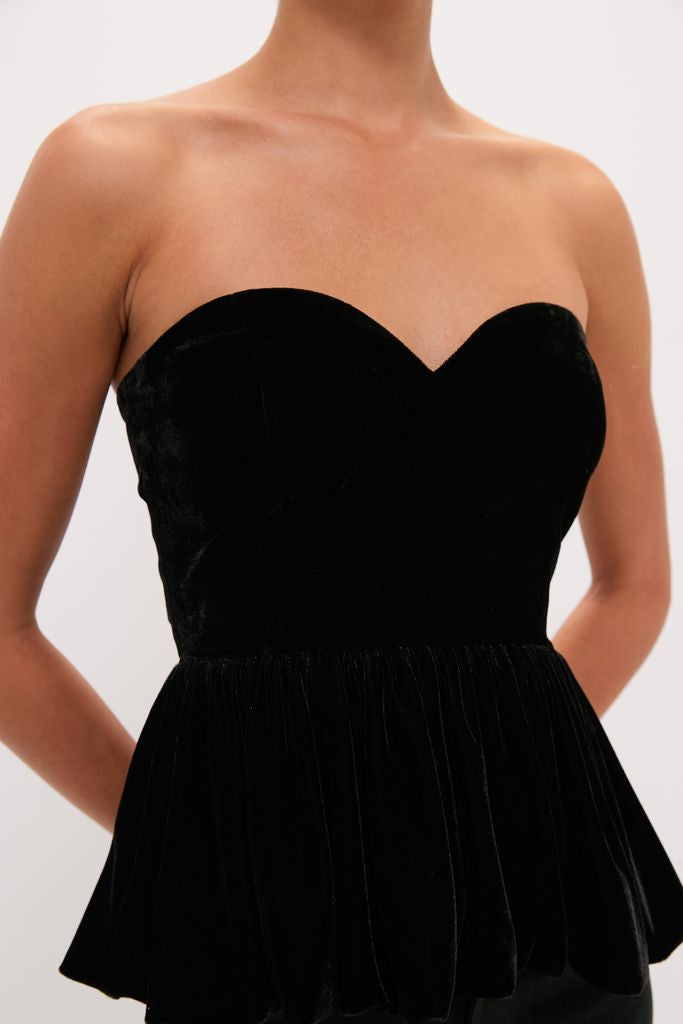 Black Velvet Peplum Strapless Tudor Blouse with a sweetheart neckline, fitted bodice, and flared hem, embodying a classic, effortless, and high-end style for a fun look.