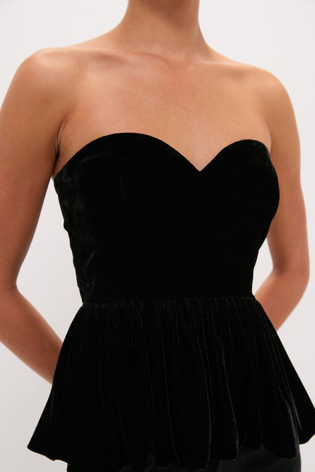 Black Velvet Peplum Strapless Tudor Blouse with a sweetheart neckline, fitted bodice, and flared hem, embodying a classic, effortless, and high-end style for a fun look.