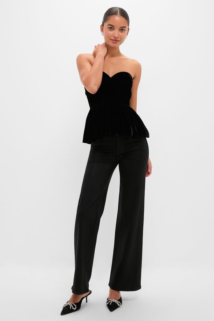 Woman models a classic, high-end Black Velvet Peplum Strapless Tudor Blouse, paired with wide-leg trousers and rhinestone-adorned heels, embodying effortless, fun sophistication.