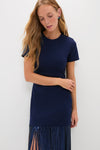 Woman in a classic Navy Sequin Fringe Stevie Midi Dress, featuring an effortless silhouette with short sleeves and a playful, high-end fringe hem. She wears colorful stud earrings.