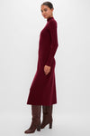 Woman models the classic Oxblood Knit Conrad Midi Swing Dress with a mock turtleneck and flared hem, paired with knee-high leather boots for an effortless, high-end look.
