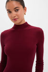 Woman wearing a classic, high-end Oxblood Knit Conrad Midi Swing Dress sweater, showcasing effortless style with a fitted ribbed design and mock-neck, complemented by a fun, small gold hoop earring.