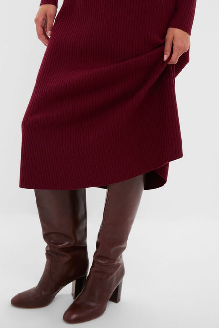 Person wearing the Oxblood Knit Conrad Midi Swing Dress, a classic ribbed design, paired with knee-high, brown leather heeled boots, embodying an effortless and high-end style.