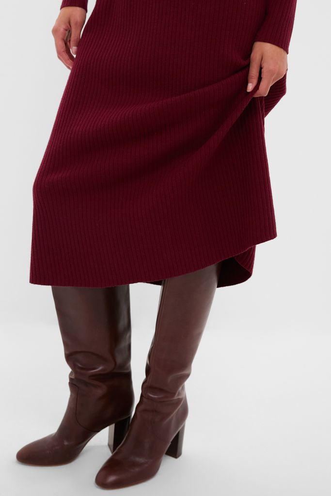 Person wearing the Oxblood Knit Conrad Midi Swing Dress, a classic ribbed design, paired with knee-high, brown leather heeled boots, embodying an effortless and high-end style.