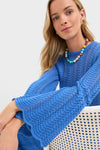 Young woman in an effortless, classic cobalt-blue crochet sweater with scalloped bell sleeves, embodying the high-end, fun style of the Cerulean Knit Comporta Midi Dress.