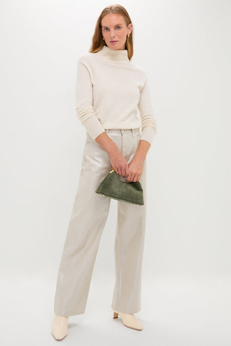Model in classic Champagne Luster Tate High Rise Bowed Wide Leg trousers, paired with an ivory turtleneck and ankle boots, holding a green suede pouch. Effortlessly high-end and fun.