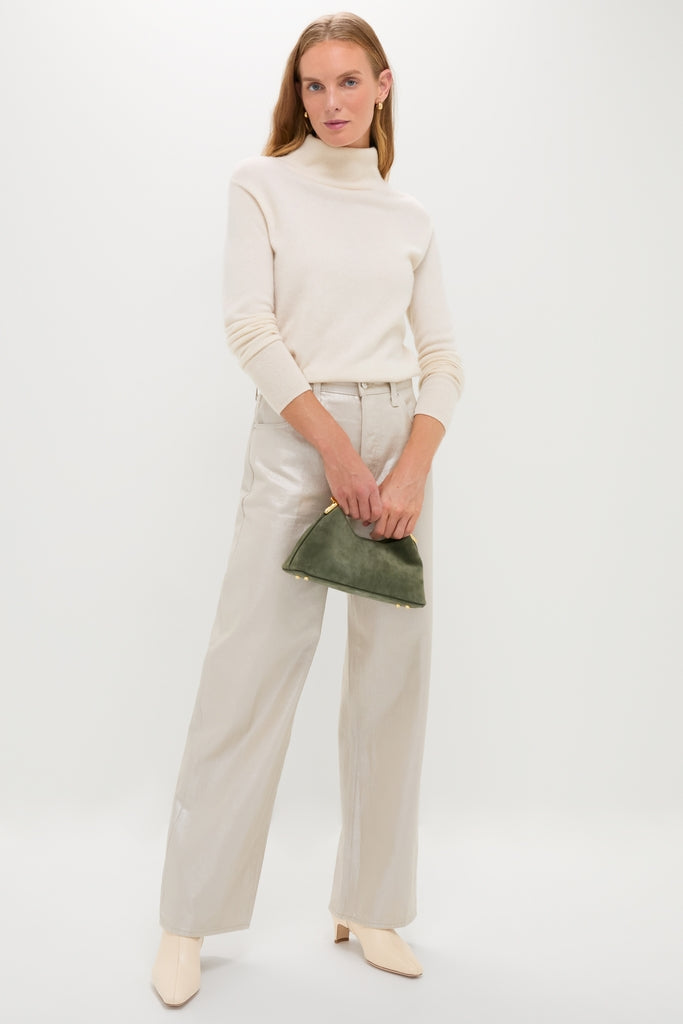 Model in classic Champagne Luster Tate High Rise Bowed Wide Leg trousers, paired with an ivory turtleneck and ankle boots, holding a green suede pouch. Effortlessly high-end and fun.