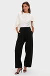 Woman models Night Out Eden Pleated Ponte Trouser, showcasing high-rise, wide-leg elegance with sharp pleats. Effortlessly combines classic tailoring with modern, high-end style.