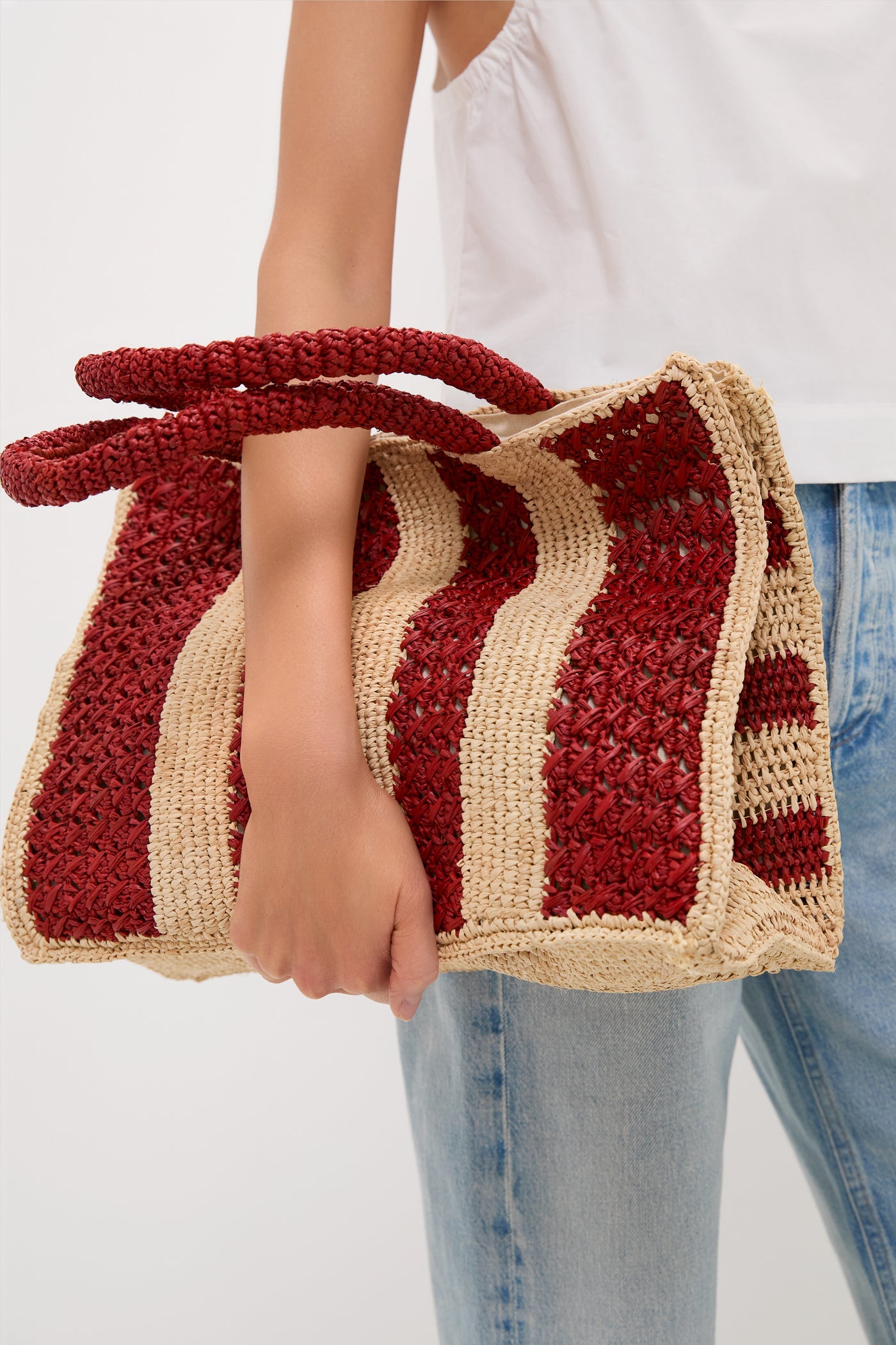 Person holding the Natural and Rust Serena Large Striped Tote, showcasing its classic, effortless design with a fun, high-end winged silhouette and braided handles.