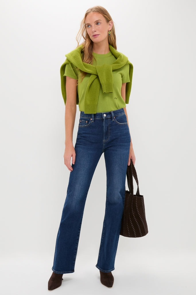 Woman models Penthouse Evie High Rise Slim Boot jeans with a classic, effortless style. Paired with a bright pullover, suede boots, and tote, showcasing high-end fashion versatility.