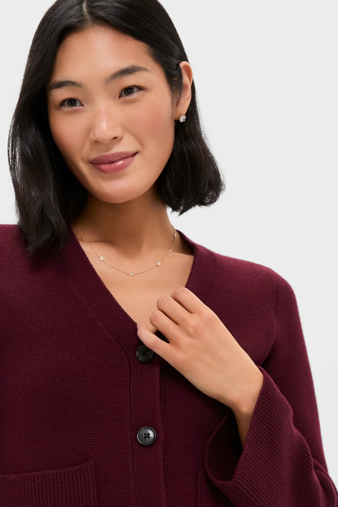 Woman wearing Claret Aeron V-Neck Cardigan, classic button-up style, effortlessly chic with patch pockets. She accessorizes with delicate gold jewelry, exuding a high-end, fun look.