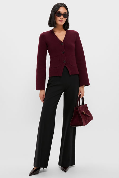 Model wearing classic Claret Aeron V-Neck Cardigan with patch pockets, paired with black wide-leg trousers, dark heels, oversized sunglasses, and a matching burgundy tote, exuding effortless elegance.