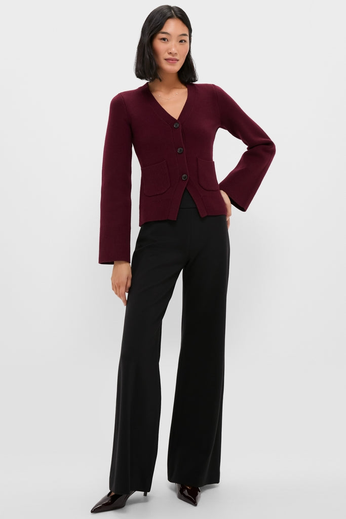 Woman wearing Claret Aeron V-Neck Cardigan with classic button-front and patch pockets, paired with high-waisted trousers, embodying an effortless, high-end, and fun style.