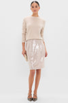 Woman models classic Champagne Sequin Clayton Midi Skirt with grosgrain waistband, styled effortlessly with a light beige sweater and chic heels, exuding high-end, fun elegance.