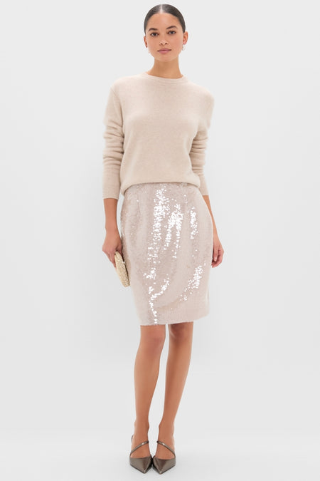 Woman models classic Champagne Sequin Clayton Midi Skirt with grosgrain waistband, styled effortlessly with a light beige sweater and chic heels, exuding high-end, fun elegance.