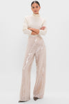 Model in classic, high-end Champagne Sequin Tatum Pants with high-rise, wide-leg design. Paired with a cream turtleneck, conveying an effortless, fun, and elegant style.