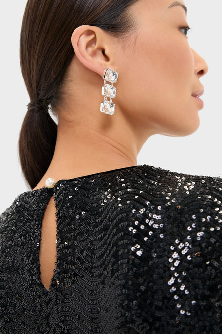 Woman in classic Black Sequin Roya Swing Mini Dress with a keyhole back, exuding an effortless, high-end look, complemented by elegant drop earrings for a fun evening out.