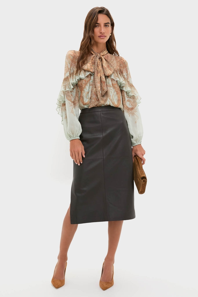 Model wearing the classic Demitasse Leather Elene Midi Skirt, paired with an effortless paisley-print blouse, holding a fun suede clutch, embodying a high-end, confident look.