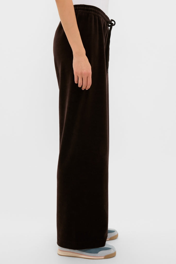 Classic side view of Chocolate Brown Velour Jane Pant, showcasing its effortless, high-end relaxed fit, wide-leg silhouette, paired with white top and blue sneakers.
