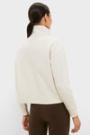 Back view of a model in a classic, cream Snap Neck Brooke Pullover with a high collar and ribbed cuffs, paired with brown leggings for an effortless, high-end look.
