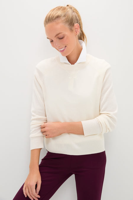 Woman wearing the classic Buttercream Washable Cashmere Malcolm Crewneck, effortlessly styled with burgundy pants. This high-end, fun sweater features raglan sleeves and embroidered details.