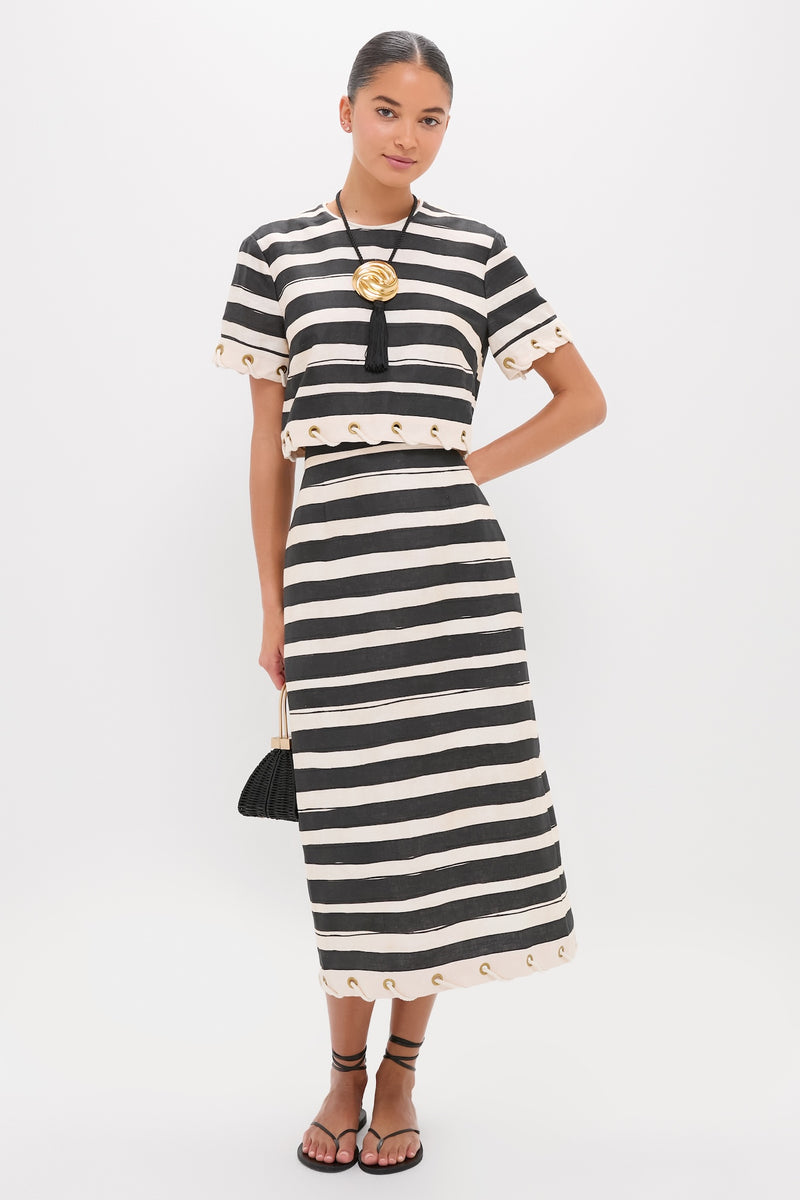 Model in classic, effortless Black Stripe Story Pencil Skirt with eyelet details, paired with matching top, gold pendant, black wicker handbag, and tie-around sandals.