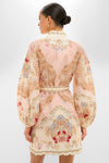 Back view of a woman in the Wallpaper Floral Blush Daylight Mini Dress, showcasing its classic, effortless elegance with ornate floral pattern, billow sleeves, and cinched waist.