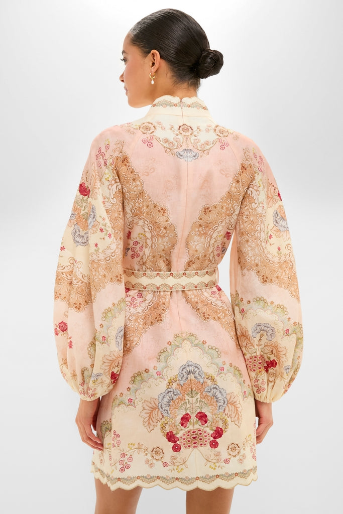 Back view of a woman in the Wallpaper Floral Blush Daylight Mini Dress, showcasing its classic, effortless elegance with ornate floral pattern, billow sleeves, and cinched waist.
