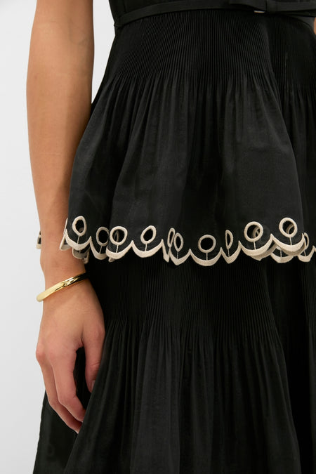 Classic Black Embroidered Tiered Midi Dress featuring a pleated skirt, scalloped embroidery, and a gold bangle, exuding an effortless high-end style perfect for fun occasions.