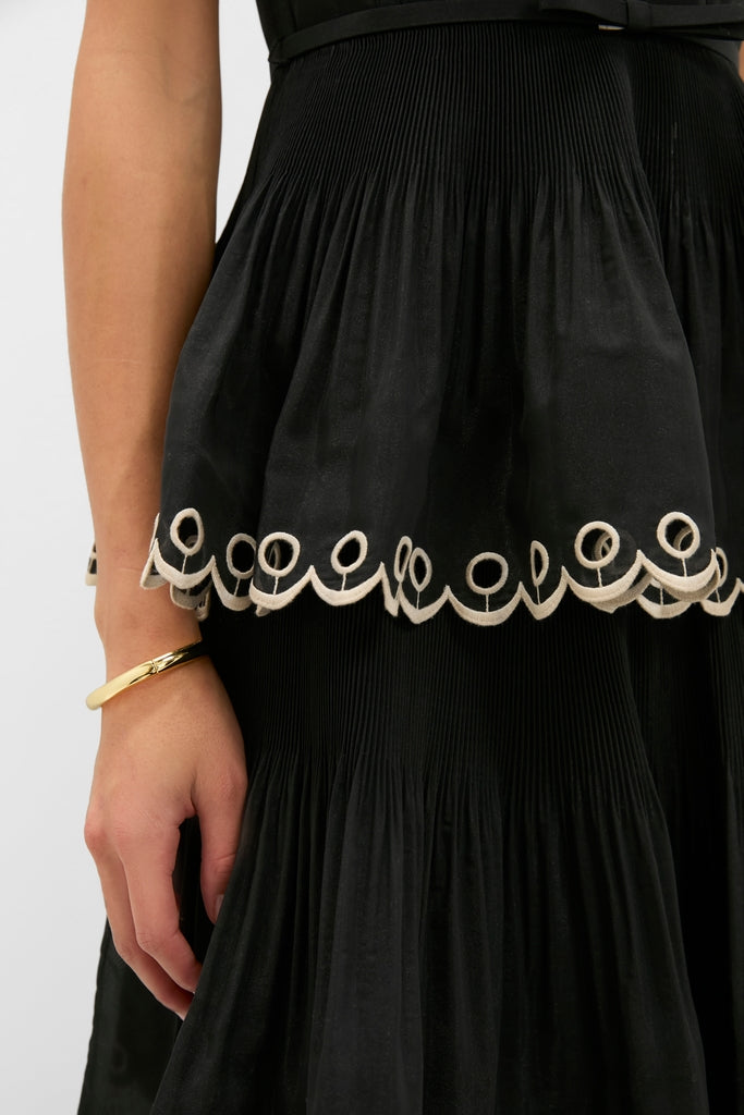 Classic Black Embroidered Tiered Midi Dress featuring a pleated skirt, scalloped embroidery, and a gold bangle, exuding an effortless high-end style perfect for fun occasions.