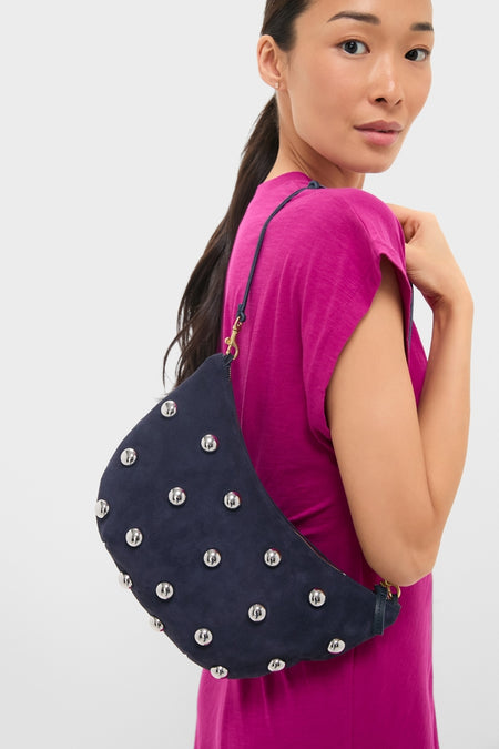 Woman in a bright dress with a classic, high-end Navy Suede Lune Bag featuring silver studs and gold-tone hardware, exuding an effortless, fun style.