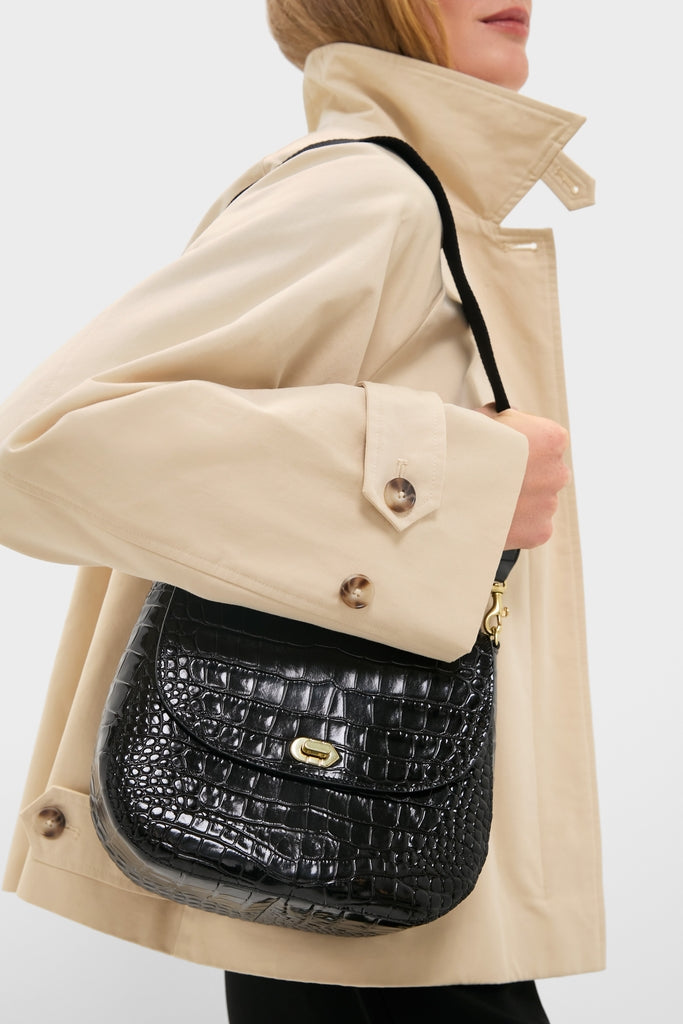 Person wearing a classic beige trench coat carries the Black Croco Turnlock Louis with Top Handle, an effortless and high-end crocodile-embossed leather shoulder bag with a gold-tone clasp.