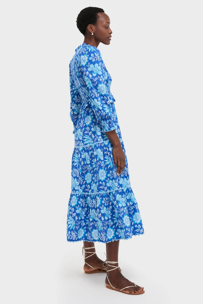Woman in profile wearing the classic Ink Jaal Mia Dress, an effortless blue tiered midi-dress with floral motifs, paired with fun, high-end lace-up sandals.