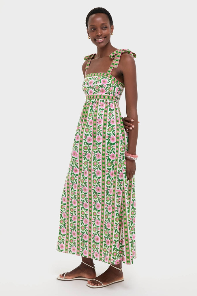 Model wearing the classic Emerald Border Mykonos Dress, featuring effortless vertical foliage and floral stripes, an empire waist, and adjustable tie straps, paired with fun white sandals.