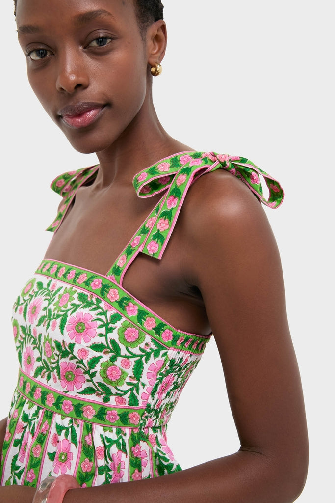 Woman wearing the Emerald Border Mykonos Dress, featuring classic, effortless embroidery of green vines and pink flowers, with bows on shoulder straps, exuding a fun, high-end style.