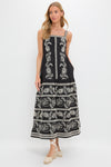 Young woman models the Sweetheart Rio Dress, a classic, high-end black maxi with white folk-inspired embroidery, an empire waist, tiered skirt, and effortless side pockets.