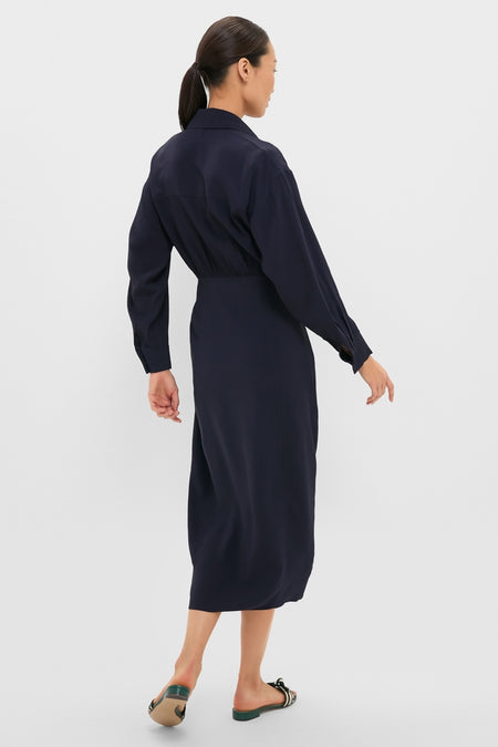 Woman models the classic, effortless Midnight Alessandra Sarong Shirt Dress, a high-end navy-blue midi with gathered waist, paired with fun striped slide sandals.