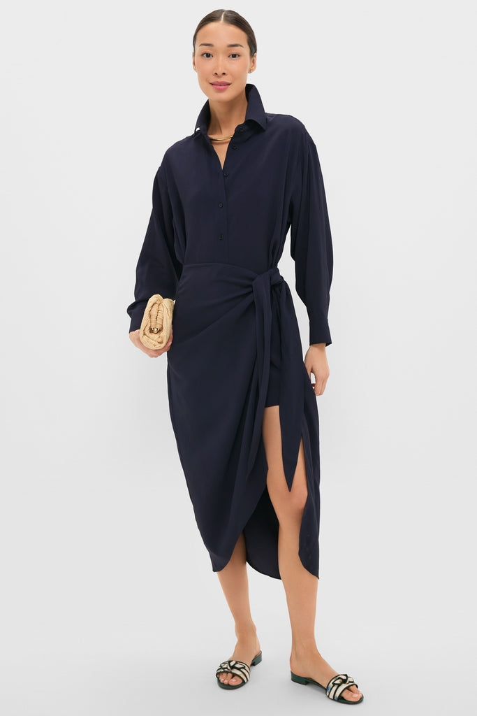 Woman models the classic Midnight Alessandra Sarong Shirt Dress with an effortless wrap-style skirt, holding a fun woven clutch and wearing high-end braided slide sandals.