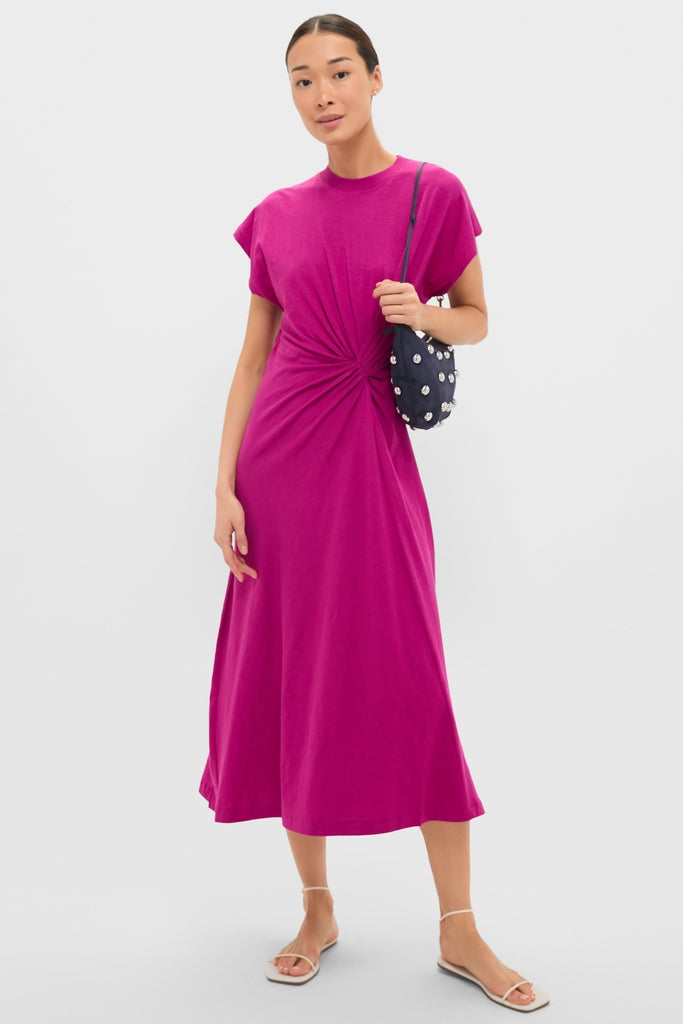 Model wearing the Fuchsia Volta Twist Dress, a classic, effortless midi with a gathered waist detail, paired with a fun cross-body bag and high-end strappy sandals.
