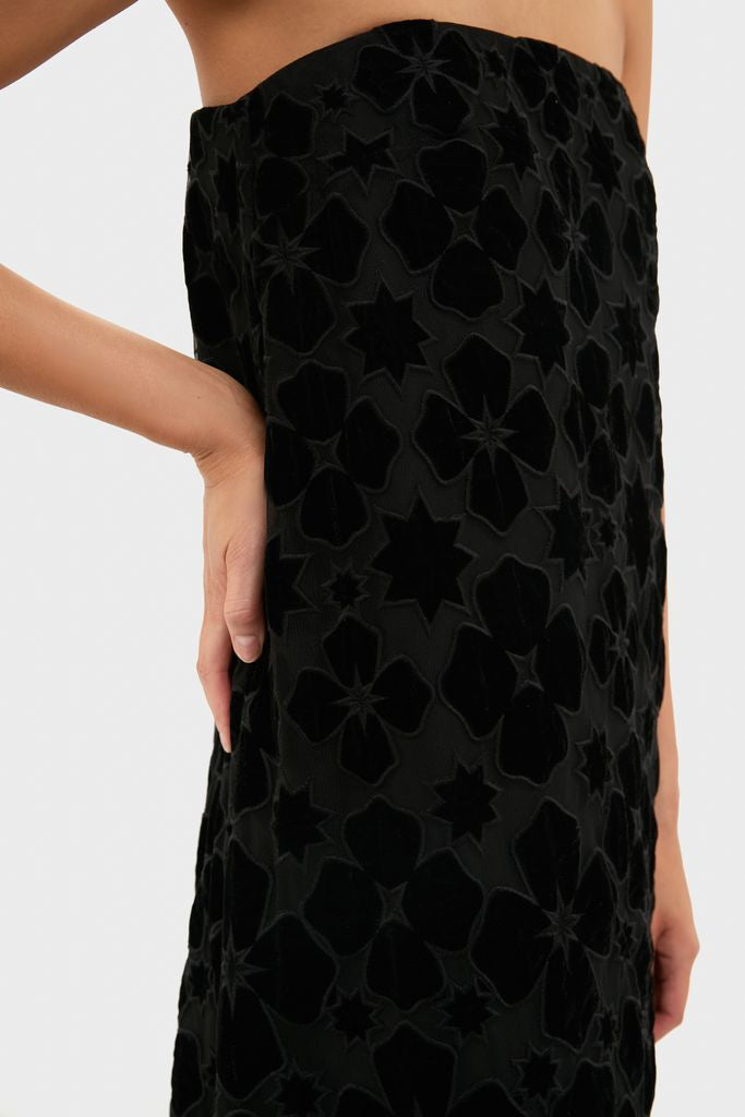 Model wearing the classic Black Burnout Velvet Genevieve Gown, featuring an effortless strapless design with a high-end, subtle floral pattern. Hand rests stylishly at waist.