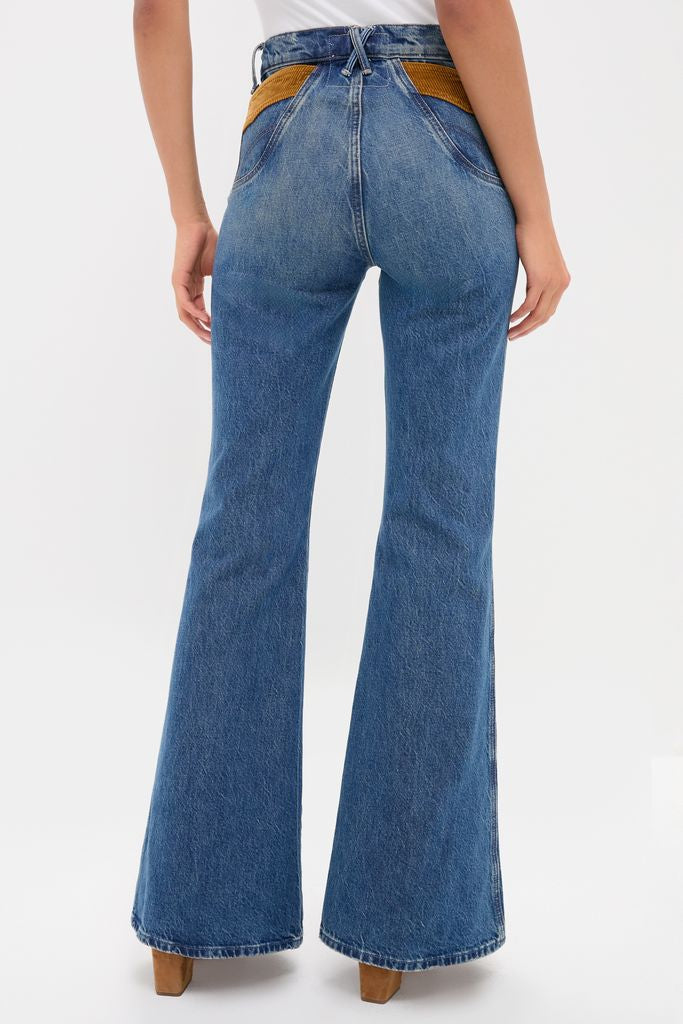 Model showcases classic, high-waisted flared blue denim jeans with pointy pocket detail, embodying an effortless, fun, high-end style.