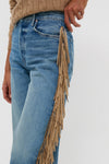 Person wearing classic light-washed denim jeans with tan suede fringe detail, styled with an effortless cable-knit sweater. Folk Star The Fringe Half-Pipe Button Sneak exudes fun, high-end appeal.