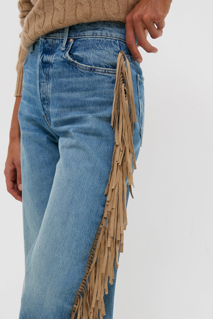 Person wearing classic light-washed denim jeans with tan suede fringe detail, styled with an effortless cable-knit sweater. Folk Star The Fringe Half-Pipe Button Sneak exudes fun, high-end appeal.