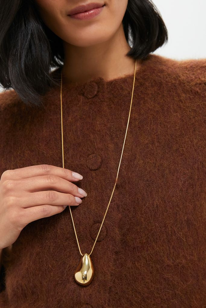 Woman wearing a classic, high-end Gold Betty Necklace with an abstract pendant, effortlessly complementing her fuzzy cardigan, embodying fun and versatile style for any occasion.