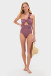 Model wears the Acai Rodriguez One Piece, showcasing a classic, high-end design with an asymmetrical rosette strap, cut-out detail, and ruching. Effortless and fun accessorizing with a sun hat.