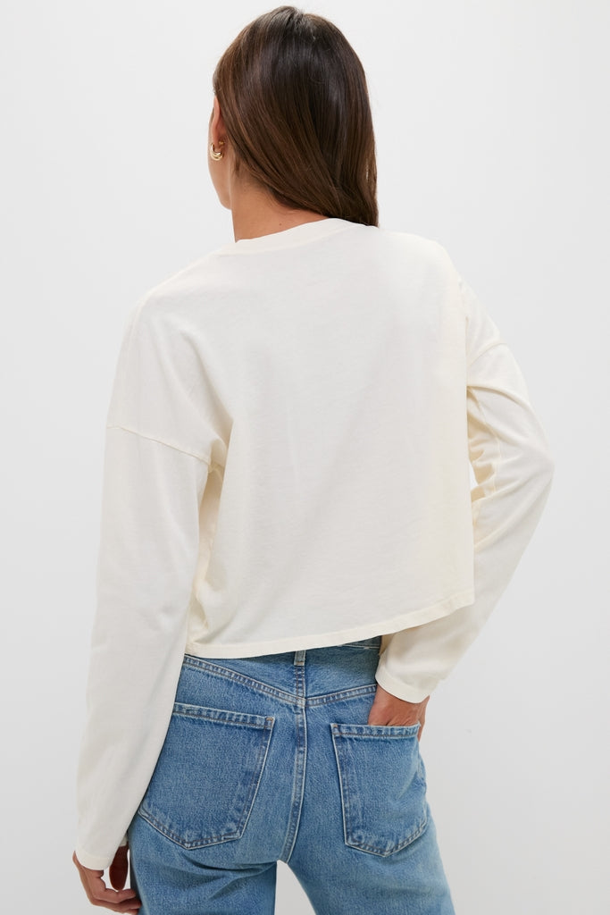 Person in a Martini Soup Crop Long Sleeve Tee, effortlessly styled with classic medium-wash jeans. Ideal for a fun, high-end, and timeless wardrobe addition.