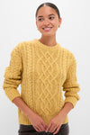 Young woman in a classic, chunky mustard-yellow Sunflower Madelyn Sweater, showcasing its effortless, high-end cable-knit design with ribbed cuffs and hem.