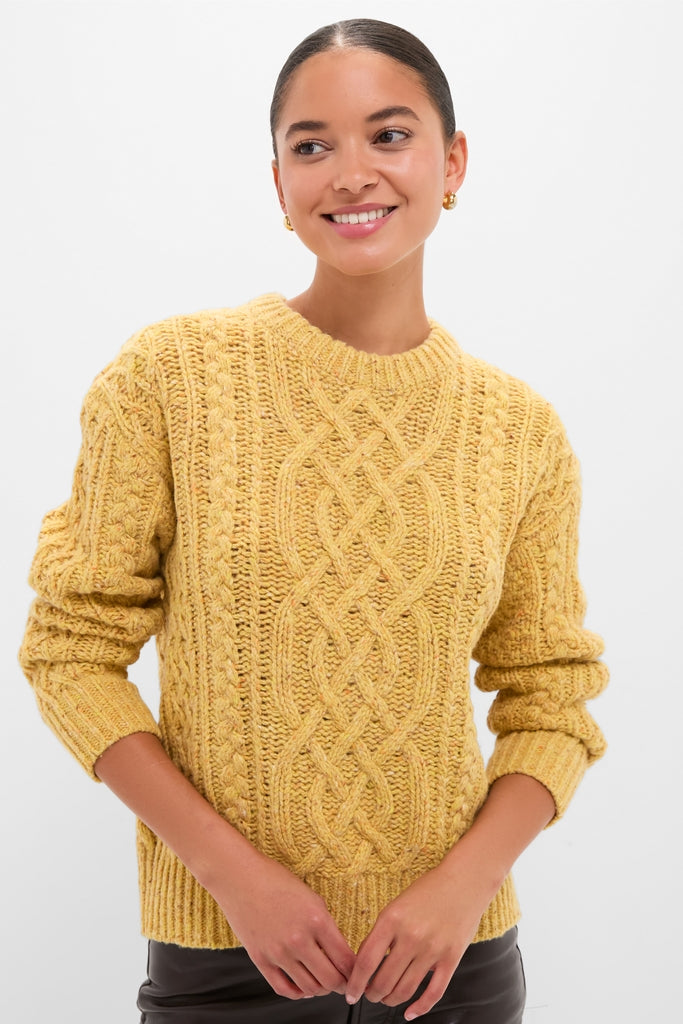 Young woman in a classic, chunky mustard-yellow Sunflower Madelyn Sweater, showcasing its effortless, high-end cable-knit design with ribbed cuffs and hem.